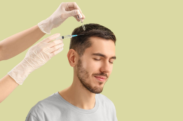 Hombre joven recibiendo tratamiento para el crecimiento del cabello sobre fondo verde, primer plano - Foto, imagen