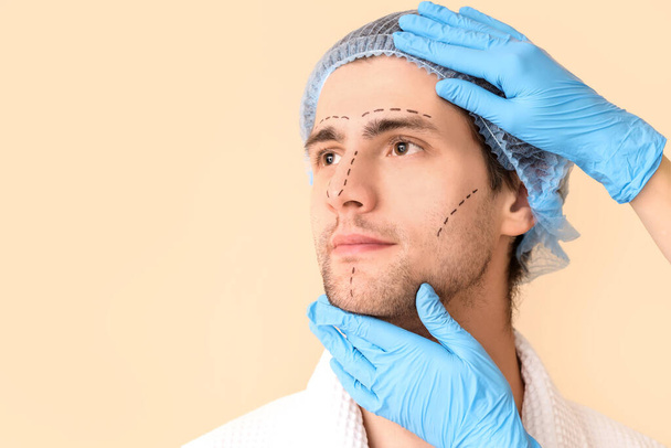 Plasztikai sebész és fiatal férfi jelölt arc bézs háttér, közelkép - Fotó, kép