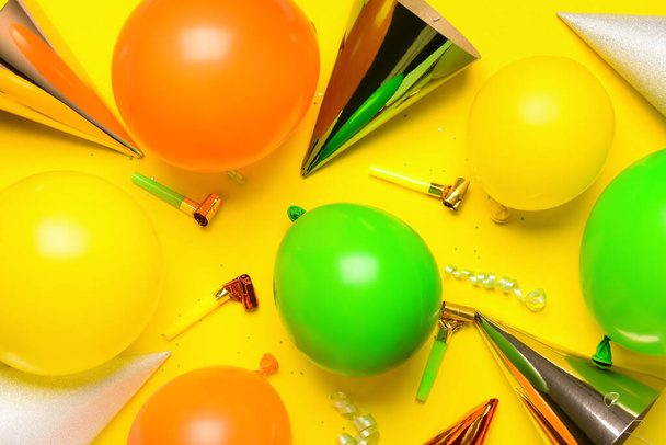 Μπαλόνια, κομφετί, θορυβώδεις μηχανές και καπέλα για πάρτι σε κίτρινο φόντο - Φωτογραφία, εικόνα