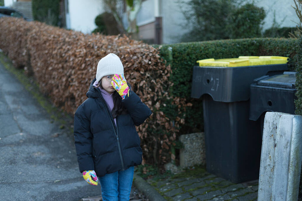 Маленька дівчинка з маскою на обличчі дивиться на смітник - Фото, зображення