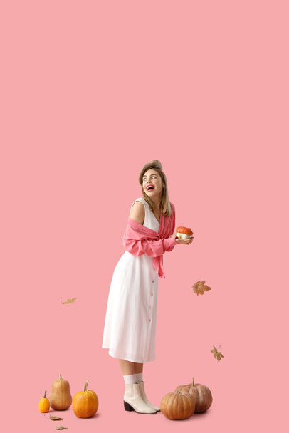 Beautiful young woman with pumpkins on pink background - Photo, Image