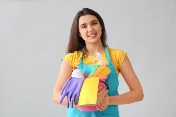 Молода жінка з прибиральними приладдям на сірому фоні - Фото, зображення