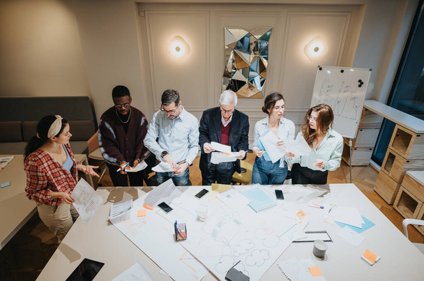 Un grupo multigeneracional de profesionales de negocios que participan en una reunión colaborativa en una oficina moderna y bien iluminada, discutiendo sobre documentos y diagramas. - Foto, imagen