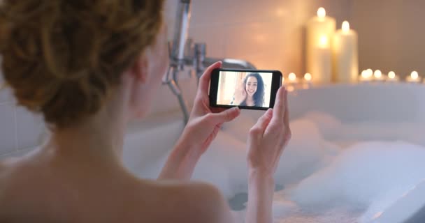 Жінка, розслабитися і відеодзвінок зі смартфоном у ванні з бульбашками, свічками і доглядом за собою вдома. Друзі, спілкуйтеся і хвилюйтеся привіт людині в прямому ефірі з телефоном, соціальними мережами або онлайн-спілкуванням. - Кадри, відео