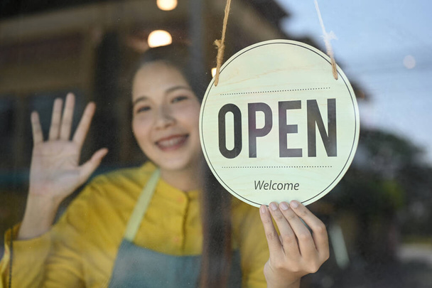 Femme souriante propriétaire de petite entreprise portant tablier tournant signe ouvert sur la porte en verre. - Photo, image