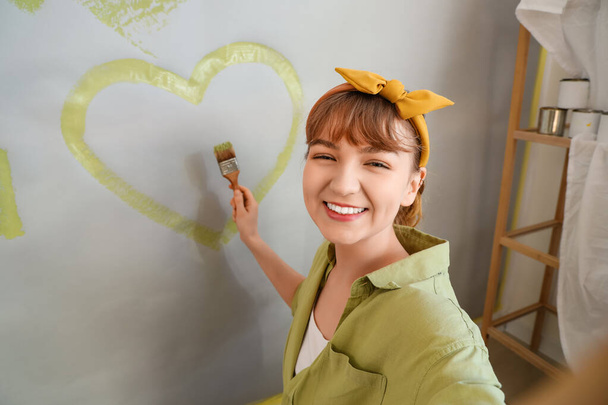 Giovane donna che disegna il cuore sul muro durante la riparazione in camera, primo piano - Foto, immagini