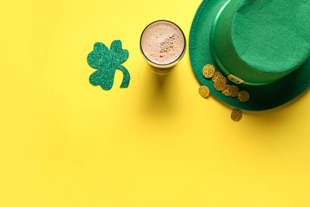 Glass of dark beer with leprechaun hat, coins and clover for St. Patrick's Day celebration on yellow background - Photo, Image