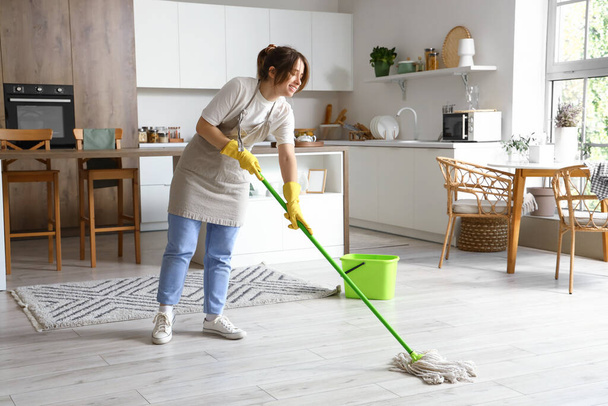 Jolie jeune femme sol de nettoyage dans la cuisine moderne - Photo, image