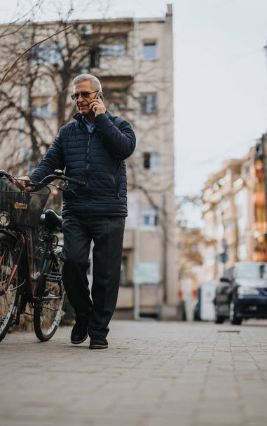 Maduro homem falando no telefone inteligente andando ao lado de bicicleta na rua da cidade. - Foto, Imagem