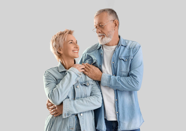 volwassen paar in denim jassen knuffelen op lichte achtergrond - Foto, afbeelding