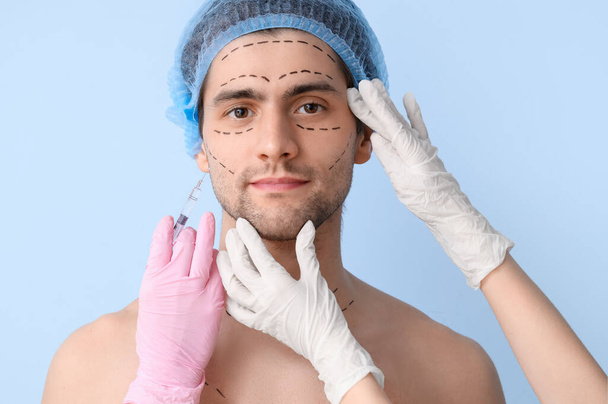 Cirujanos plásticos con jeringa y hombre joven con la cara marcada sobre fondo azul, primer plano - Foto, imagen