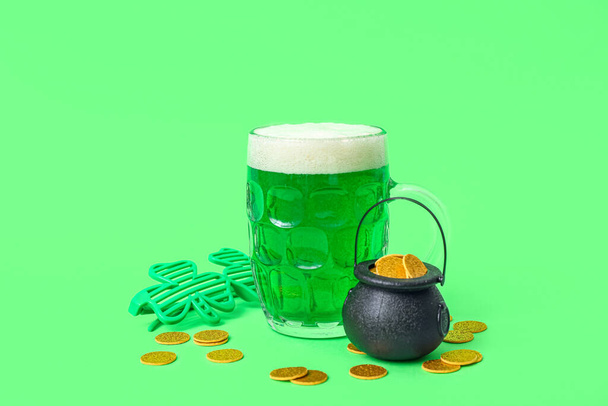 Стакан пива с монетами и декоративными стаканами на зеленом фоне. Празднование Дня Святого Патрика - Фото, изображение