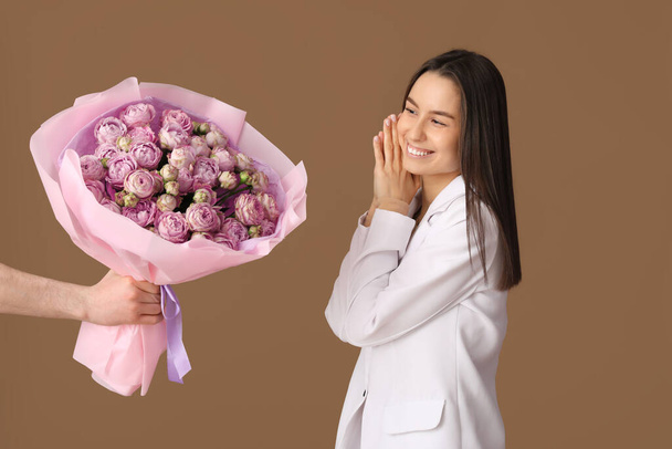 Jeune femme recevant un bouquet de belles roses sur fond brun - Photo, image