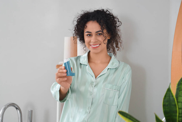 Uśmiechnięta młoda Afroamerykanka z inhalatorem astmy w łazience - Zdjęcie, obraz
