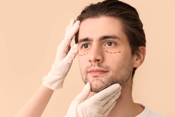 Plasztikai sebész és fiatal férfi jelölt arc bézs háttér, közelkép - Fotó, kép