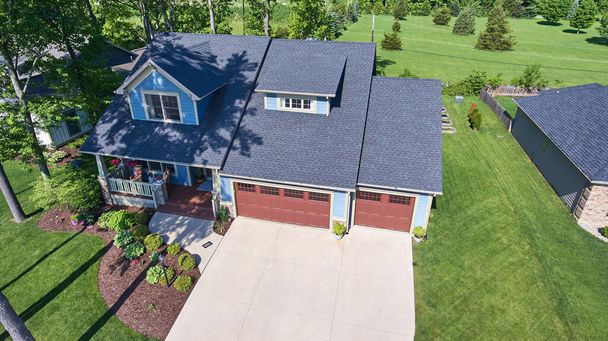 Vista aérea de una encantadora casa suburbana de dos pisos con fachada azul y puertas de garaje rojas en Fort Wayne, Indiana, que muestra un paisaje bien cuidado y un barrio sereno. - Foto, Imagen