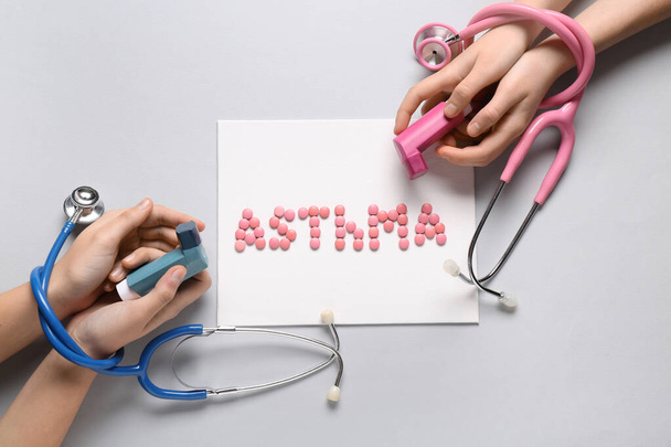 Mãos de criança com inaladores, estetoscópios e palavra ASTHMA feita de comprimidos sobre fundo branco - Foto, Imagem