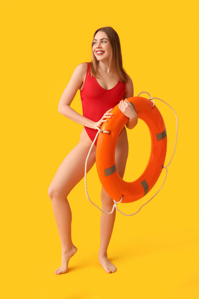 Beautiful young woman in tank swimsuit and with lifebuoy on yellow background - Photo, Image