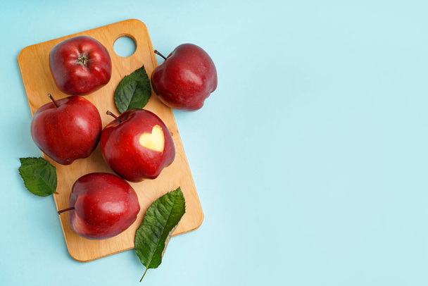 Ahşap tahta tahta tahta tahta üzerinde oyulmuş kalp ve mavi arka plan yaprakları olan kırmızı elmalar. - Fotoğraf, Görsel