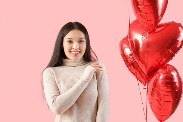 Молода азіатка з повітряними кульками у формі серця на день Святого Валентина на рожевому фоні - Фото, зображення