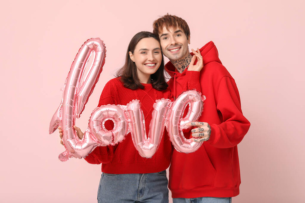 ピンクの背景に愛という言葉の形をしたエアバルーンを持つ若いカップル. バレンタインデーのお祝い - 写真・画像