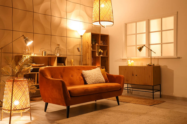 Interior de la elegante sala de estar con lámparas brillantes y sofá por la noche - Foto, imagen