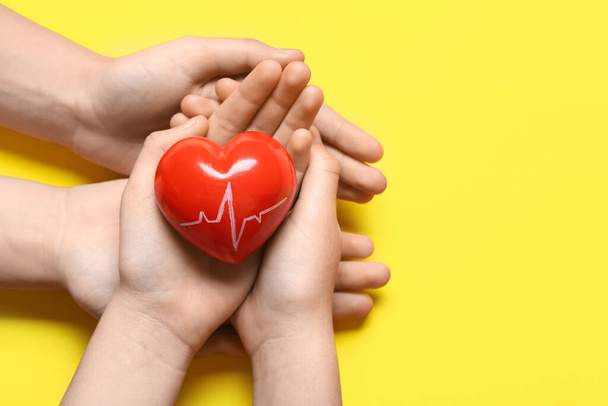 黄色い背景に心臓検査で赤い心臓を保持する女性と子供の手 - 写真・画像