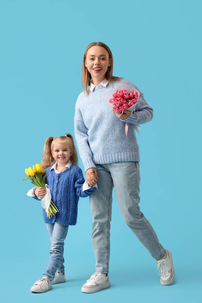 Dziewczynka z matką i bukietami tulipanów na niebieskim tle. Międzynarodowy Dzień Kobiet - Zdjęcie, obraz