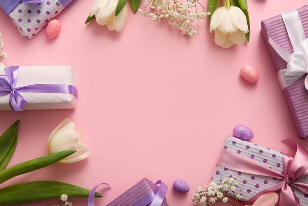 Kehys valmistettu pääsiäismunista kukkia ja lahjapakkauksia vaaleanpunaisella taustalla - Valokuva, kuva