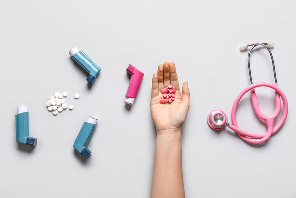 Child's hand with asthma inhalers, pills and stethoscope on white background - Photo, Image