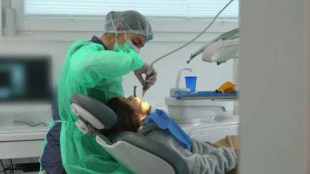 Концентрированная женщина-стоматолог лечит детские зубы в клинике. Профессиональный персонал - Фото, изображение
