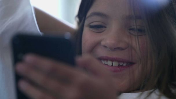 Boldog gyermek nevetve hangosan reagál a tartalom az interneten, miközben nézi a mobiltelefon eszköz. Közelkép a kislány nevet a vicces szórakoztató média - Fotó, kép