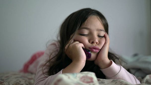 Одна споглядальна молода дівчина з сумним виразом відчуває легку нудьгу, тримаючи голову руками в підборідді, 8-річна дитина лежить у ліжку думаючи нічого не робити - Фото, зображення