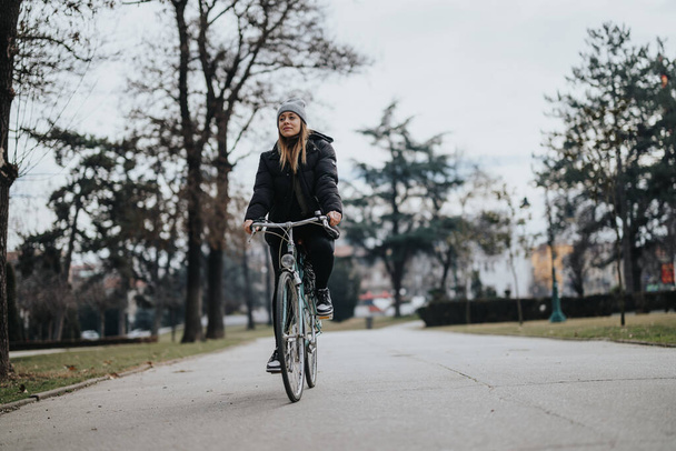 Nuori naispyöräilijä kulkee puistopolkua pitkin puiden ja luonnon ympäröimänä ja nauttii aktiivisesta elämäntavasta ja vapaa-ajasta ulkona.. - Valokuva, kuva