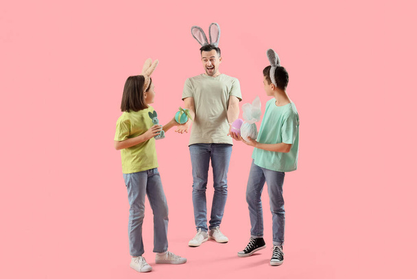 Pienet lapset ja hänen isänsä pupukorvissa, joilla on pääsiäismunia vaaleanpunaisella taustalla - Valokuva, kuva