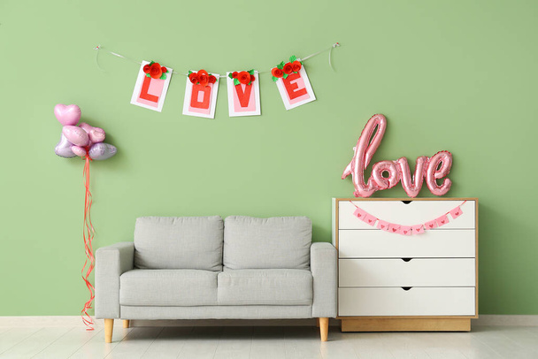 Interior of festive living room with grey sofa, heart-shaped balloons and bunting with word LOVE. Valentine's Day celebration - Photo, Image