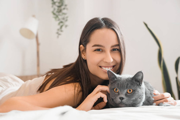 Jonge vrouw met schattig Brits Stenografisch kat liggend op bed thuis, close-up - Foto, afbeelding