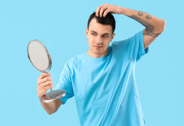Jeune homme avec problème de perte de cheveux et miroir sur fond bleu - Photo, image
