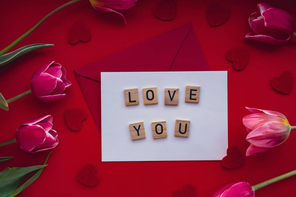 MIŁOŚĆ SMS na kopercie z pięknym różowym bukietem tulipanowym na czerwonym tle. Makieta szablonu świątecznej kartki z życzeniami. Romans miłość Walentynki Top view Flat lay Kobieca koncepcja - Zdjęcie, obraz