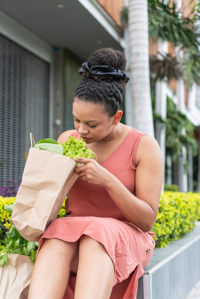 Een vrouw inhaleert de frisse geur van haar boodschappen, wiebelt een zak met levendige greens. - Foto, afbeelding