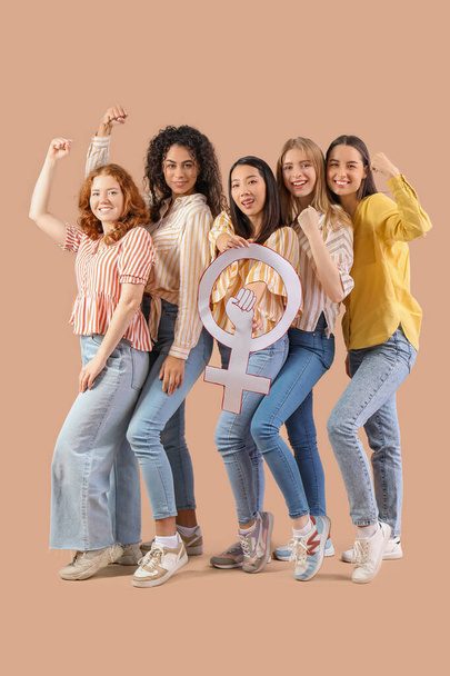 Beautiful young women with clenched fists holding gender symbol on beige background. Women history month - Photo, Image