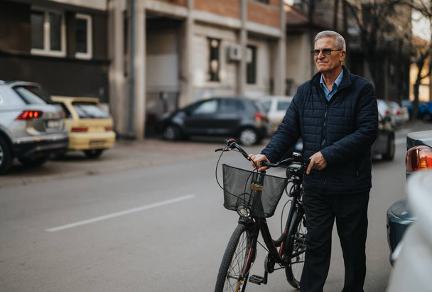 Cavalheiro idoso ativo desfruta de um estilo de vida saudável, posando com sua bicicleta em uma estrada urbana, mostrando independência e fitness. - Foto, Imagem