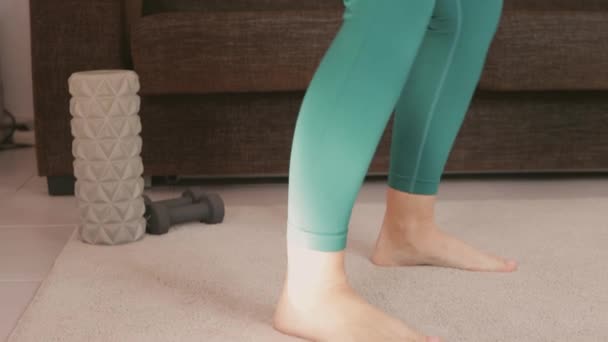 Femme athlétique s'entraînant à faire des squats et des fentes à la maison dans le salon. Fille sportive à l'entraînement. Entraînement et exercices physiques avec une corde, bande élastique de remise en forme. Concept sportif - Séquence, vidéo