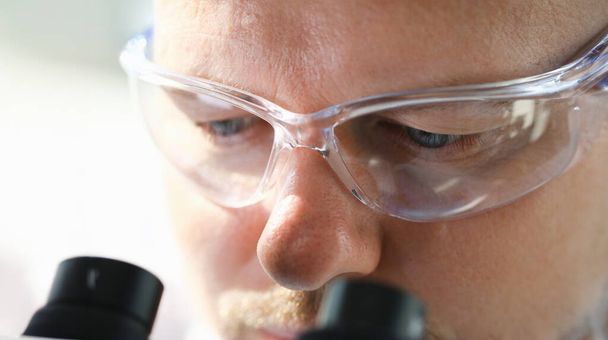 Красива людина вчений, дивлячись через бінокулярний мікроскоп, вивчає хвороби вірусу, який заражає водою vivo IVf
 - Фото, зображення