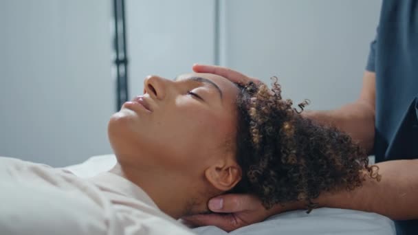 Tıbbi merkezde yatan hastalar için masaj seansı. Bilinmeyen fizyoterapist, kadına baş ağrısı baskısı uyguluyor. Kıvırcık Afrikalı Amerikalı, osteopati kliniğinde rehabilitasyonda rahatlıyor. - Video, Çekim
