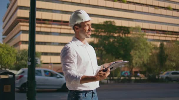 サンビーム市のクローズアップで建物の計画をチェックする集中エンジニア. サマーストリートでウォルキー・トーキーを使って 青写真を手にした男を 計画した。 屋外で作業する指示を与える真剣なコンストラクター - 映像、動画