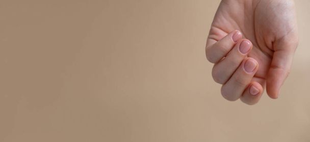 中立ベージュの背景にスタイリッシュなヌードベージュの女性の爪. 現代流行のスタイリッシュな美しいマニキュア. かわいいパステルネイル美容治療の最小限のデザインコンセプト. ジェルネイル。 スキンケア - 写真・画像