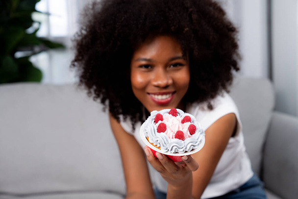 Schöne junge afrikanische Bloggerin präsentiert Cupcake mit selektivem Fokus auf Konzeptküche. Content-Erstellung von sozialen Medien online mit Lieblings-Süßigkeiten Bäckerei Gericht. Geschmacksmacher. - Foto, Bild