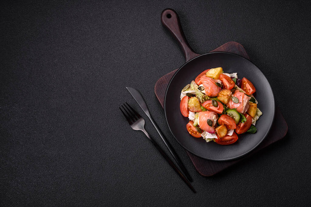 Delicious juicy salad with salmon, tomatoes, cucumber, herbs, pumpkin seeds, salt and spices in a ceramic plate on a dark concrete background - Photo, Image