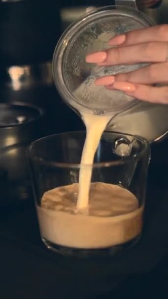 Kobiece ręce wlewające świeże mleko do kubka czarnej kawy w kafejce w biurze. zbliżenie - pionowe - Materiał filmowy, wideo